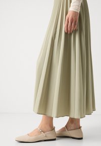 Beige ballettsko med spiss tå, stropp over vristen, og lav hæl, kombinert med et plisserte, lysegrønt skjørt.