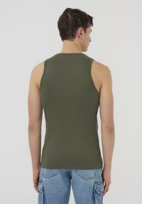 Canotta a coste verde oliva con un design aderente, scollatura rotonda e senza maniche, abbinata a pantaloni cargo blu chiaro.
