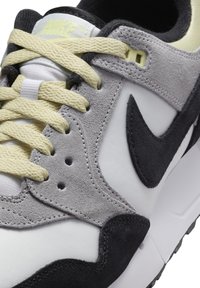 Zapatillas de deporte de ante gris y sintético negro con detalles en blanco, cordones amarillos y un swoosh negro de Nike, que cuentan con una parte superior texturizada y un collar acolchado.