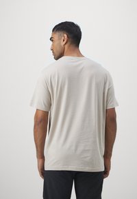 Lys beige t-skjorte i bomull med korte ermer, rund hals og en jevn tekstur. Baksiden har et enkelt, udekorerte design.