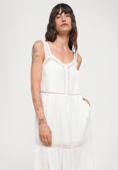 Vestido blanco sin mangas con acentos de encaje, diseño en capas y detalles de botones. Fabricado con una tela ligera y de textura suave.