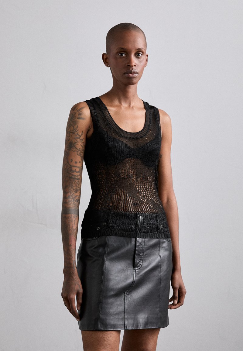 Top de tirantes de punto negro con un patrón texturizado, combinado con una minifalda de cuero negro con un acabado suave y detalle de costura en la parte delantera.