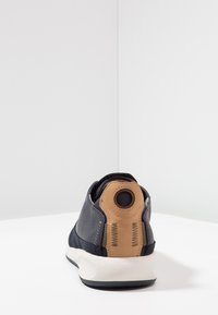 Sneaker blu navy con un accento in pelle beige sul tallone. Presenta dettagli perforati, un passante rotondo per il tallone e una suola bianca.