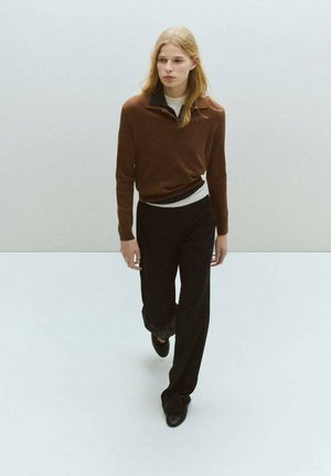 Pulóver de punto marrón con cuello negro, combinado con pantalones negros ajustados y zapatos negros. Textura suave, diseño minimalista.