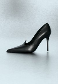Chaussure stiletto à talon haut en cuir noir avec bout pointu, présentée sur une surface lisse gris clair.