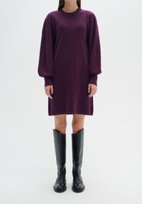 Lila överdimensionerad stickad klänning med långa, puffiga ärmar, i kombination med höga svarta läderstövlar. Slät textur, längd under knäet.