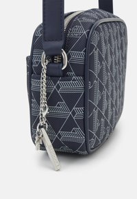 Borsa a tracolla quadrata blu navy realizzata in materiale testurizzato con motivo geometrico bianco, dotata di una cerniera argentata e di una catena con un'etichetta del marchio.