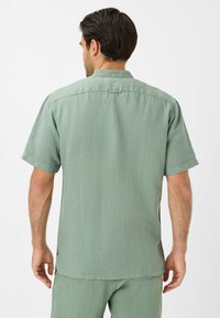 Kortearm, lichtgroen shirt van textuurstof, met een kraag, rugpas en zijsplitten voor gemakkelijke beweging.