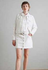Vit denimjacka och kjoloutfit, med knappdetaljer, fransade slag och ett matchande vitt bälte. Slät textur, avslappnad passform.