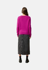 Fuchsia gebreide trui met een ronde hals en raglanmouwen, gecombineerd met een zwarte denim midi rok met een centrale achteropening. Zwarte schoenen.