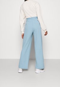 Helle blaue weit geschnittene Hose aus strukturiertem Stoff mit elastischem Bund, kombiniert mit einem beigen Langarmoberteil und weißen Sneakers.