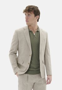 Beige Leinenanzugsjacke mit drei Knöpfen, kombiniert mit einem strukturierten olivgrünen Poloshirt. Glattes Material, taillierte Passform, keine sichtbaren Muster.