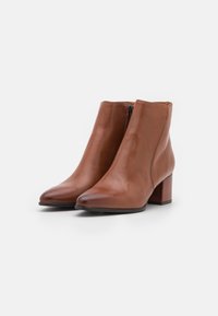 Paire de bottines en cuir marron lisse avec talons carrés et fermetures éclair latérales sur fond blanc.