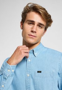 Ljusblå knappar-skjorta i denim med bröstficka och en liten svart logotag. Har klassisk krage och sydda detaljer.