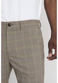 Bruna rutiga byxor med knäppning, med en strukturerad tyg och subtila kontrasterande linjer i beige. Skräddarsydd passform synlig.