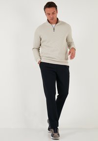 Heledad kreemjas värvitoonis pool-zip pullover ribadega, sobitatud tumedate laevavärvidega pükste ja hallide aktsentidega tossudega.