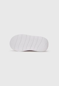 Semelle de chaussure blanche avec un motif de grip texturé en vagues et un petit logo en relief près de l'orteil, présentée sur un fond blanc uni.