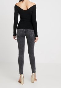 Haut noir côtelé à épaules dénudées associé à un jean taille haute gris foncé, complété par des sandales à talons hauts métalliques dorées.