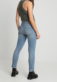 Modré džínové skinny jeans s vysokým pasem, se zadním sedlem a dvěma zadními kapsami. Nosené s zeleným topem bez rukávů a černými botami.
