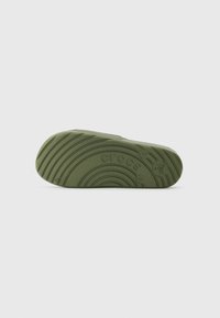 Sole in gomma verde dei Crocs con texture rigata, caratterizzata dal nome del marchio "crocs" impresso e un design a motivo circolare.