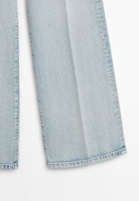 Pantalon en jean bleu clair avec jambes droites et couture apparente sur fond blanc.