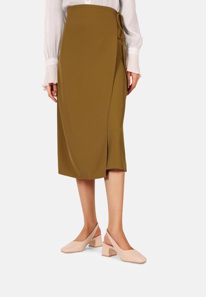 Gonna avvolgente verde oliva con chiusura laterale, lunghezza al ginocchio, indossata con decolleté rosa pallido e una blusa bianca con texture.