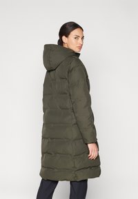 Olivově zelená zimní bunda s kapucí, se stylovým prošívaným designem, dlouhým střihem a zipovým zapínáním. Tkanina vypadá hladce a teple.