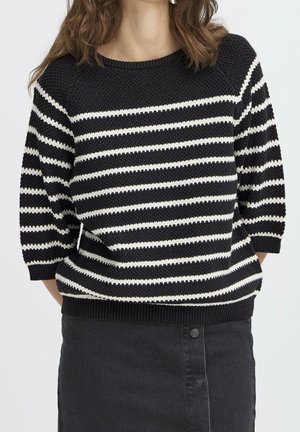 Femme portant un pull en maille rayé noir et blanc avec des manches trois-quarts et une jupe noire taille haute avec boutons sur le devant.