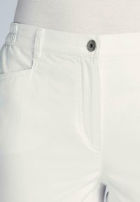 Pantalon blanc en tissu lisse, avec un fermeture à bouton et des poches latérales avec des détails de couture visibles.