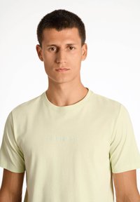 T-shirt verde chiaro a maniche corte in morbido cotone con collo tondo. Presenta un sottile logo "LINDGEBRGH" dello stesso colore sul petto.