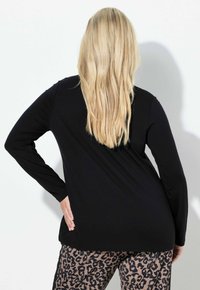 Czarna bluzka z długim rękawem o luźnym kroju, zestawiona z beżowymi spodniami w panterkę. Gładka tkanina o prostym fasonie i zaokrąglonym dole.