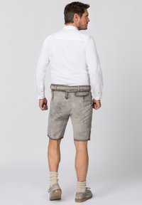 Grijze leren shorts met een gladde textuur, riemlussen en zijzakken, gecombineerd met een witte overhemden en grijze sokken en schoenen.