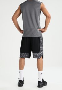 Débardeur de sport gris associé à un short noir avec un motif géométrique gris. Des chaussures de sport noires et des chaussettes blanches complètent la tenue.