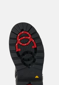 Černá gumová podrážka boty s texturovaným vzorem, zdobená červenými akcenty a stříbrnými cvočky pro lepší přilnavost a podporu.