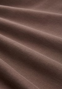 Brązowa tkanina elastyczna o gładkiej fakturze, ukazująca miękkie fałdy i subtelny połysk, idealna do zastosowań w odzieży lub tapicerce.