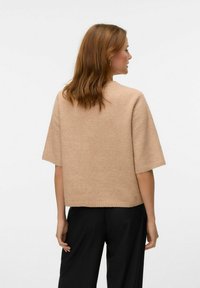 Beige gebreide trui met een brede, korte mouwontwerp, voorzien van een ronde halslijn en een ontspannen pasvorm, gecombineerd met zwarte broek.