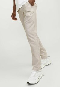Pantalones beige de corte slim, confeccionados en tela ligera. Presentan bolsillos laterales y se combinan con zapatillas deportivas blancas.