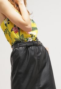 Floral-patterned yellow sleeveless top paired with a black faux leather skirt featuring an elastic waistband and a belt with gold hardware.