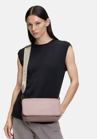 Pink leather crossbody bag with a structured shape, featuring a logo-embossed front and a soft fabric strap with brand lettering.