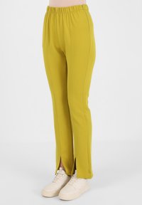 Żółte elastyczne spodnie z gumką w pasie, z bocznymi rozporkami na kostkach i kontrastowym przeszyciem. W zestawie z jasnymi trampkami.