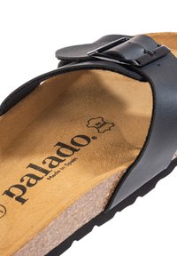 Zwarte leren sandaal met een vlakke kurken voetbed, voorzien van een zilveren gesp detail. Geprofileerde voering met "palado" in reliëf op de binnenzool.