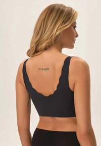 Czarny stanik z falbaniastym dekoltem i szerokimi ramiączkami. Gładki, elastyczny materiał. Ukazuje tatuaż na plecach. Prosty i minimalisty design.