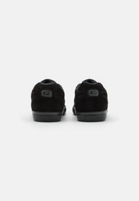 Black suede sneakers with a rubber sole. Notable rounded heel and smooth surface. Features subtle logo detail on the back.