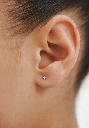 Pendiente de plata en forma de estrella con pequeñas piedras preciosas transparentes. Primer plano de una oreja que muestra el diseño y material del pendiente.