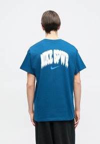 Μπλε βαμβακερό t-shirt με μεγάλο λευκό γραφικό "NIKE SPWR" και μικρό μπλε λογότυπο Nike, με χαλαρή εφαρμογή και στρογγυλή λαιμόκοψη.
