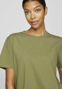 Olivgrön t-shirt med korta ärmar, tillverkat av mjuk bomull, med rund halsringning och avslappnad passform. Slät textur, inga synliga mönster eller metalldelar.