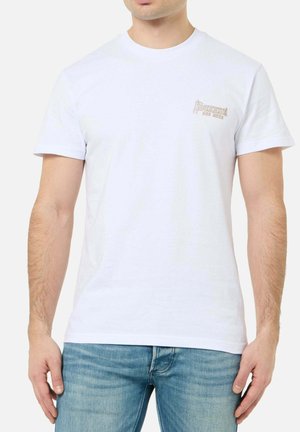 Mann trägt ein schlichtes weißes T-Shirt mit kurzen Ärmeln und kleinem beigen "Boxeur Des Rues"-Logo auf der linken Brust, kombiniert mit blauen Jeans.