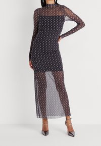 Dlouhá černá síťovaná šaty s motivem srpku měsíce, těsně přiléhající design a průhledné rukávy. Disponují vysokým výstřihem a detailem rozparku.