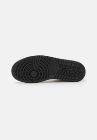 Semelle en caoutchouc noire d'une chaussure Nike montrant des motifs de bande de roulement circulaires et rectangulaires avec le logo Nike dans la section centrale.