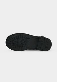 Semelle en caoutchouc noir d'une botte avec des crampons profonds et une adhérence texturée pour une meilleure traction, présentée à plat sur un fond clair uni.